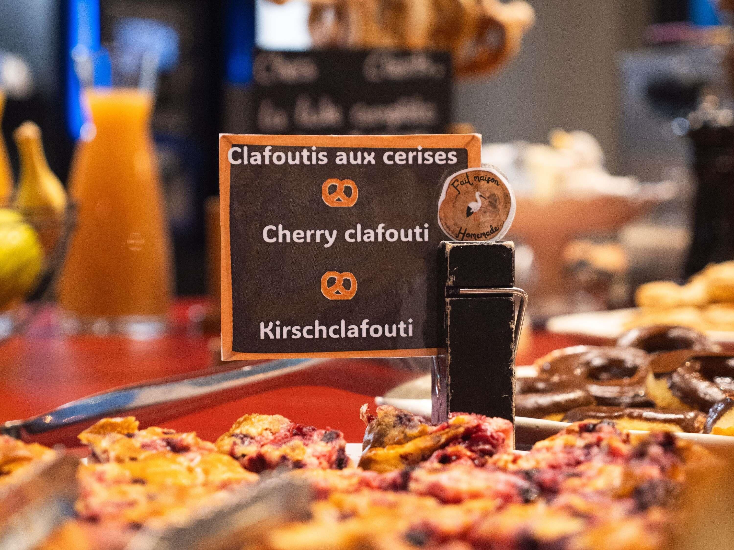 A menu board with options for clafoutis and pretzels, a knife, and various baked goods on a counter.