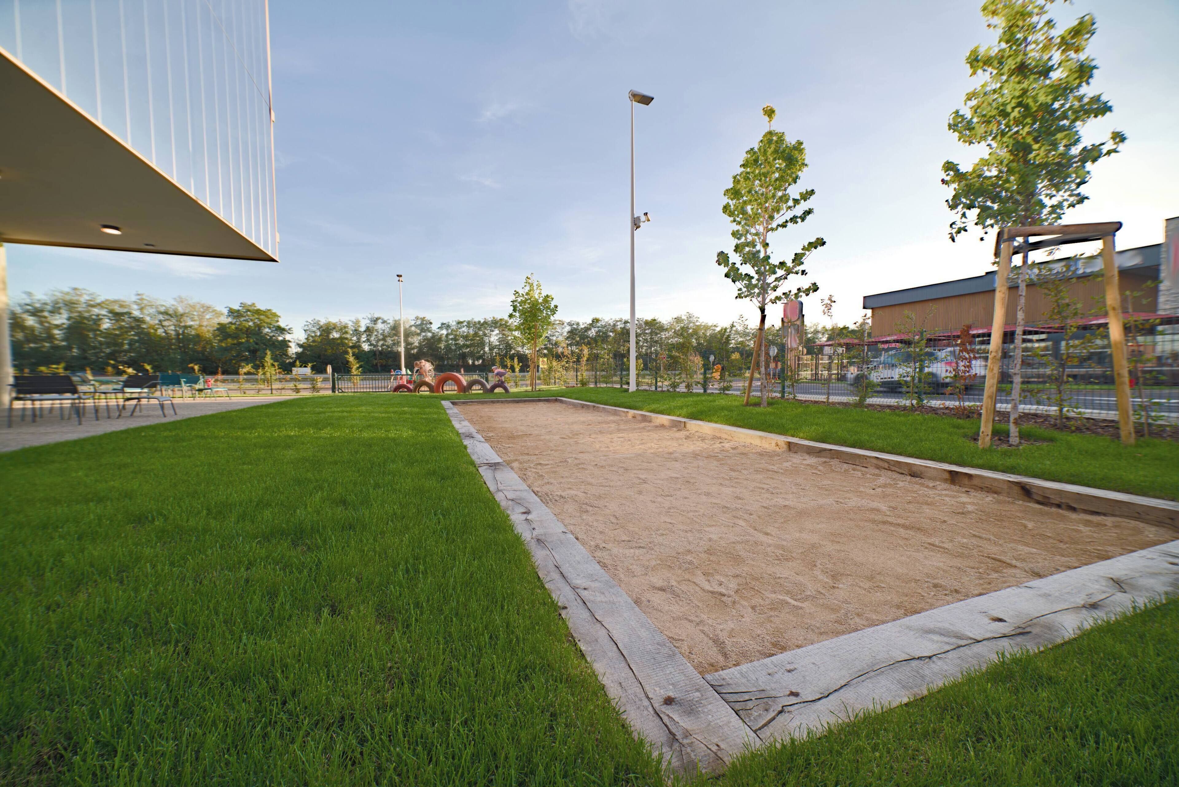 A sports court with a sandpit, surrounded by grass and trees.