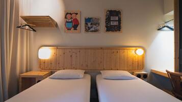 Una habitación con dos camas, cabecero de madera, lámparas fijadas a la pared, una mesita pequeña y un perchero.