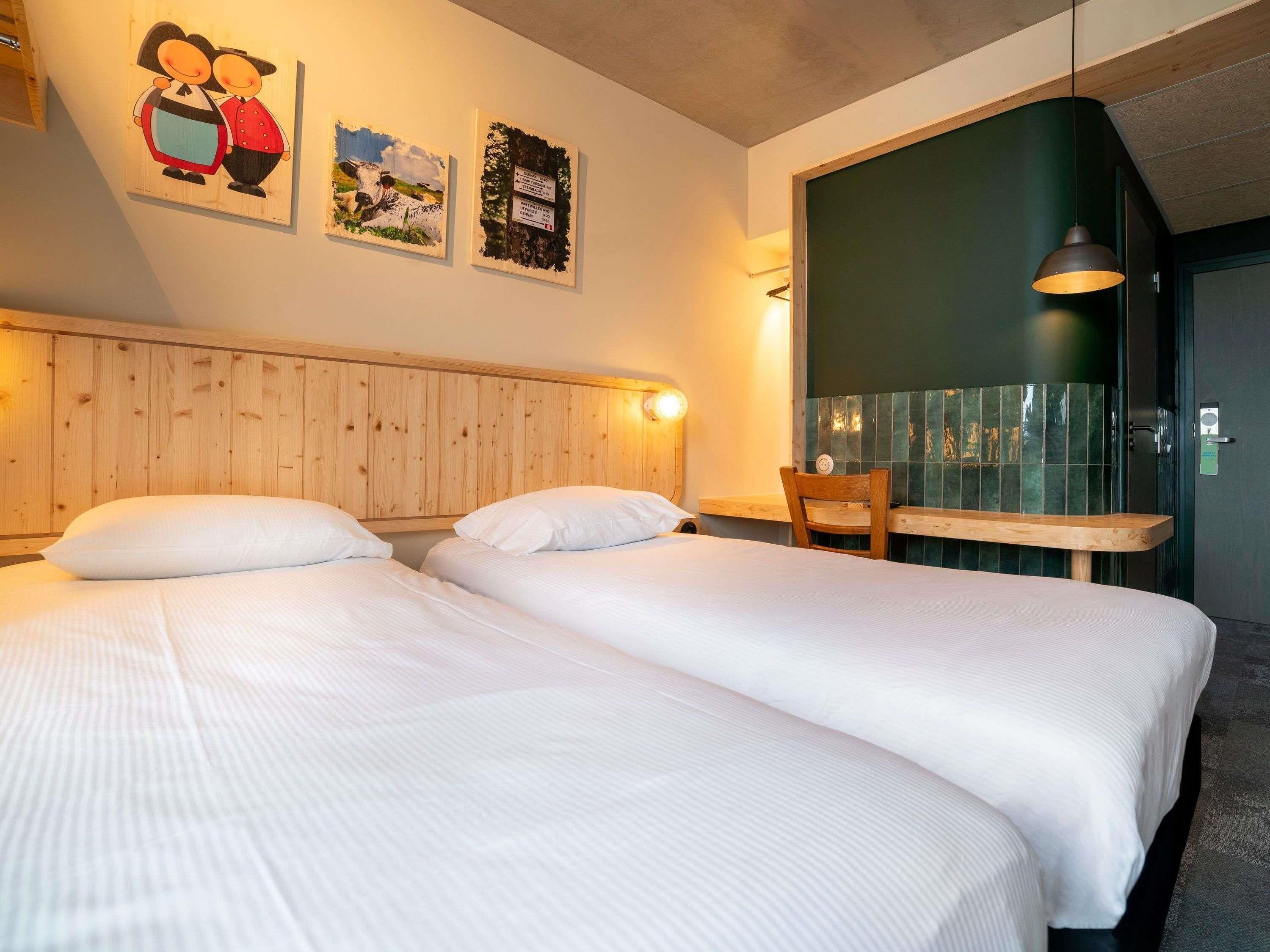 A hotel room with two beds, a wooden headboard, a wooden table, and a chair.