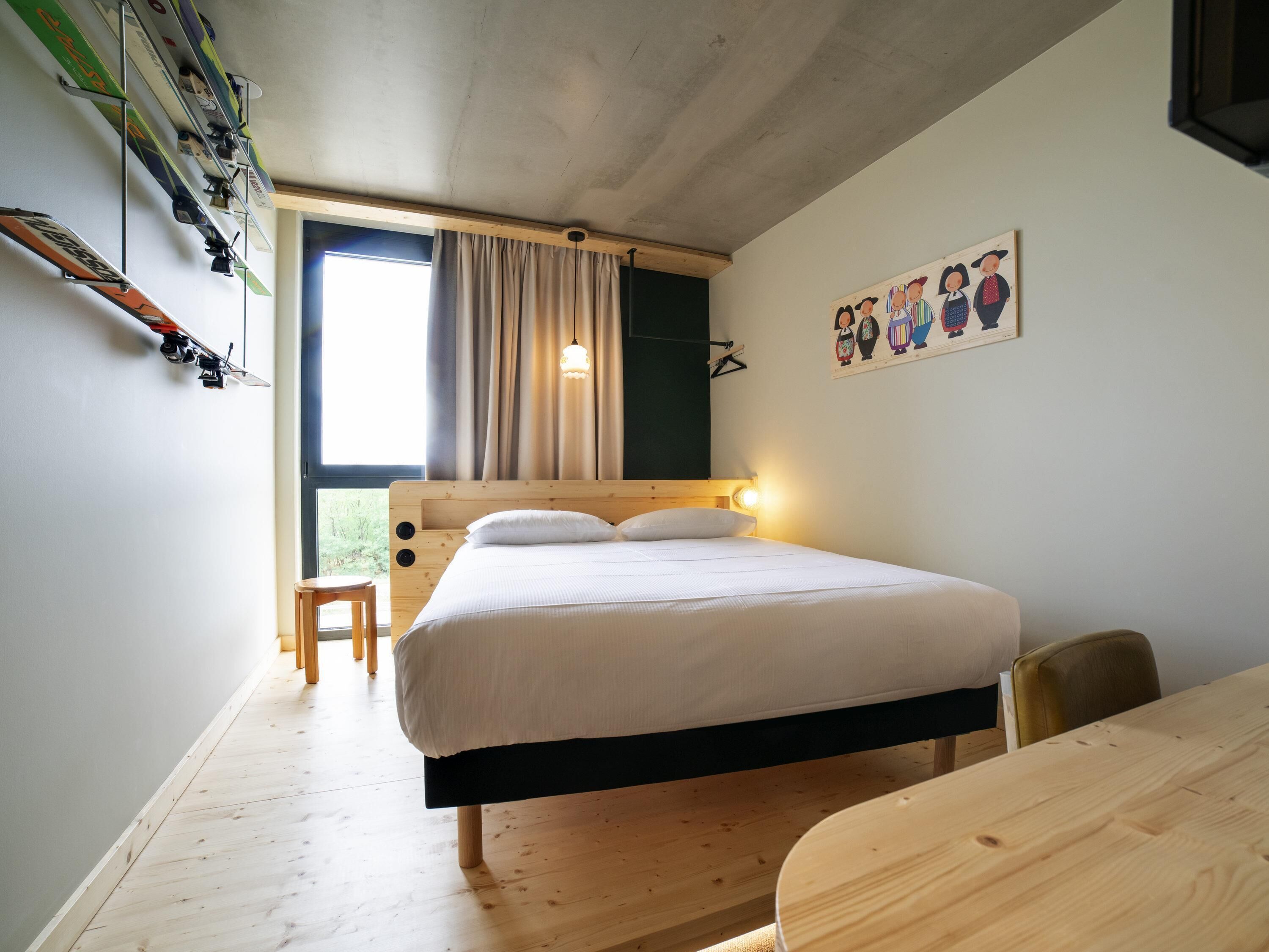A bedroom with a bed, a wooden desk, a chair, a window with curtains, and a wall-mounted picture.