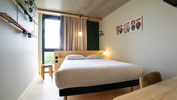 A bedroom with a bed, a wooden desk, a chair, a window with curtains, and a wall-mounted picture.