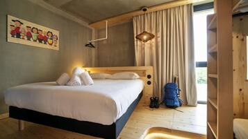 Een slaapkamer met een houten bed, een hangende lamp, een blauwe rugzak en een schilderij aan de muur.