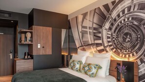 A modern bedroom with a large bed, a wall clock, and a built-in wardrobe. - Novotel Paris Val de Fontenay (Fontenay-sous-Bois)