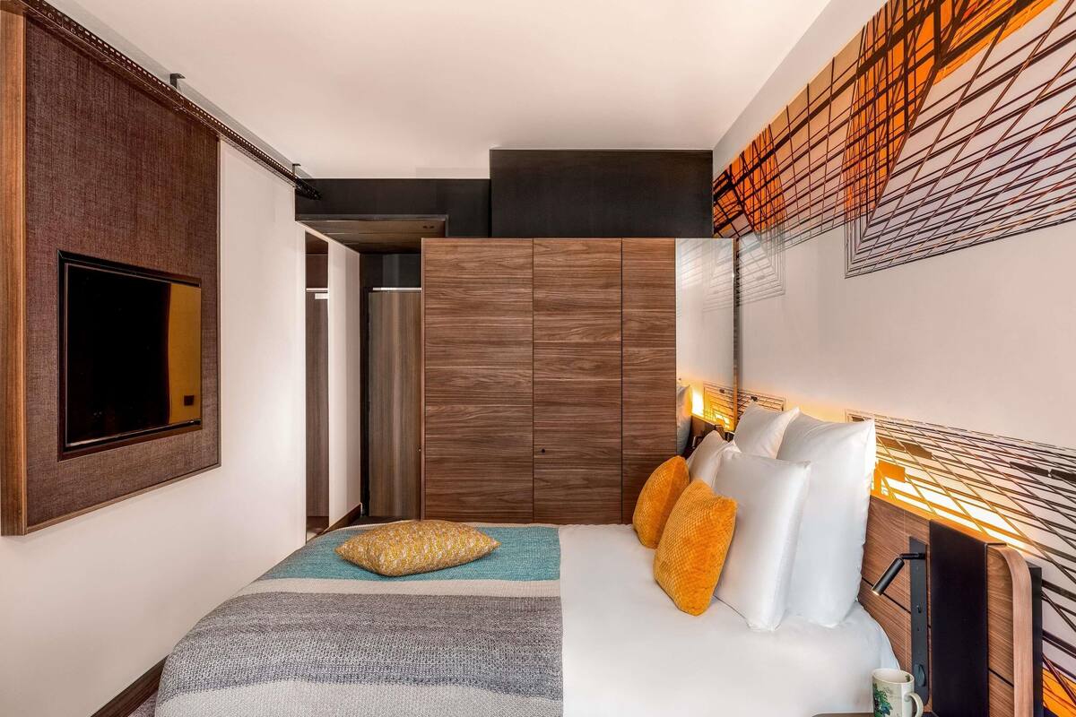 A modern hotel room with a bed, a television, a wardrobe, and a decorative wall panel.