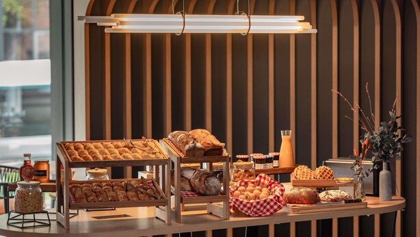 A breakfast buffet with various pastries and bread, a hanging light fixture, and a striped wall in the background. - Novotel Paris Val de Fontenay (Fontenay-sous-Bois)