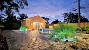 Ein Haus mit gepflasterter Auffahrt, einem Pool und einem gepflegten Garten mit verschiedenen Pflanzen.