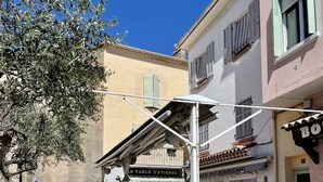 An outdoor café with stone tables and chairs, a covered seating area, and a building with a restaurant sign. - Joli Cocon au Cœur de Ville et à 2 pas des Plages (Saint-Raphaël)