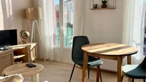 A modern living room with a wooden dining table, two chairs, a sofa, a TV, and a floor lamp. - Joli Cocon au Cœur de Ville et à 2 pas des Plages (Saint-Raphaël)
