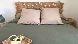 A bed with a woven headboard, two pillows, and a basket of toiletries on the bed. - Joli Cocon au Cœur de Ville et à 2 pas des Plages (Saint-Raphaël)