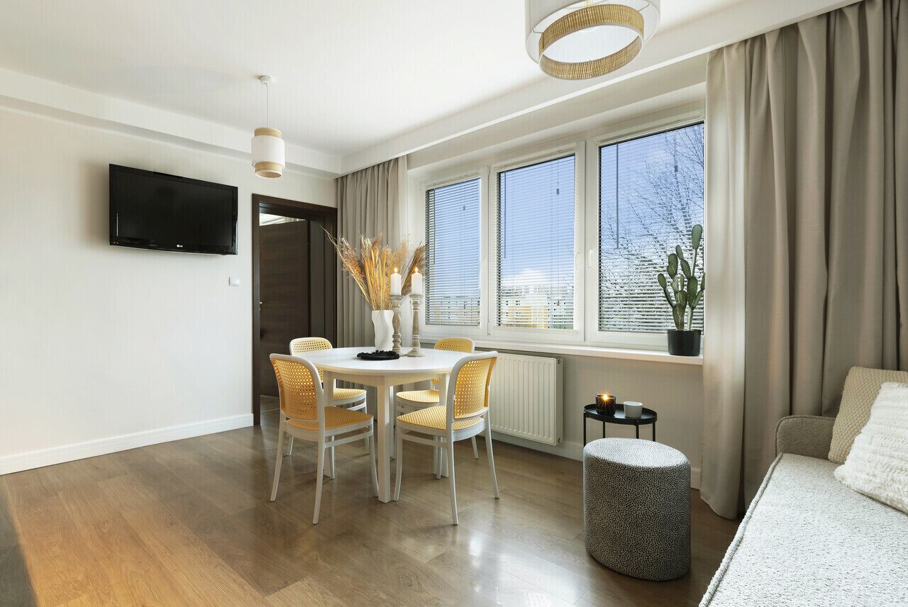 Una sala de estar moderna con comedor, ventanas amplias, un televisor de pantalla plana y una planta en maceta.