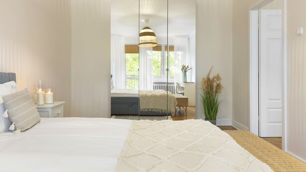 A bedroom with a large bed, a bedside table with candles, a mirror, and a view of a balcony. - Elite Apartments Sunset (Gdansk)