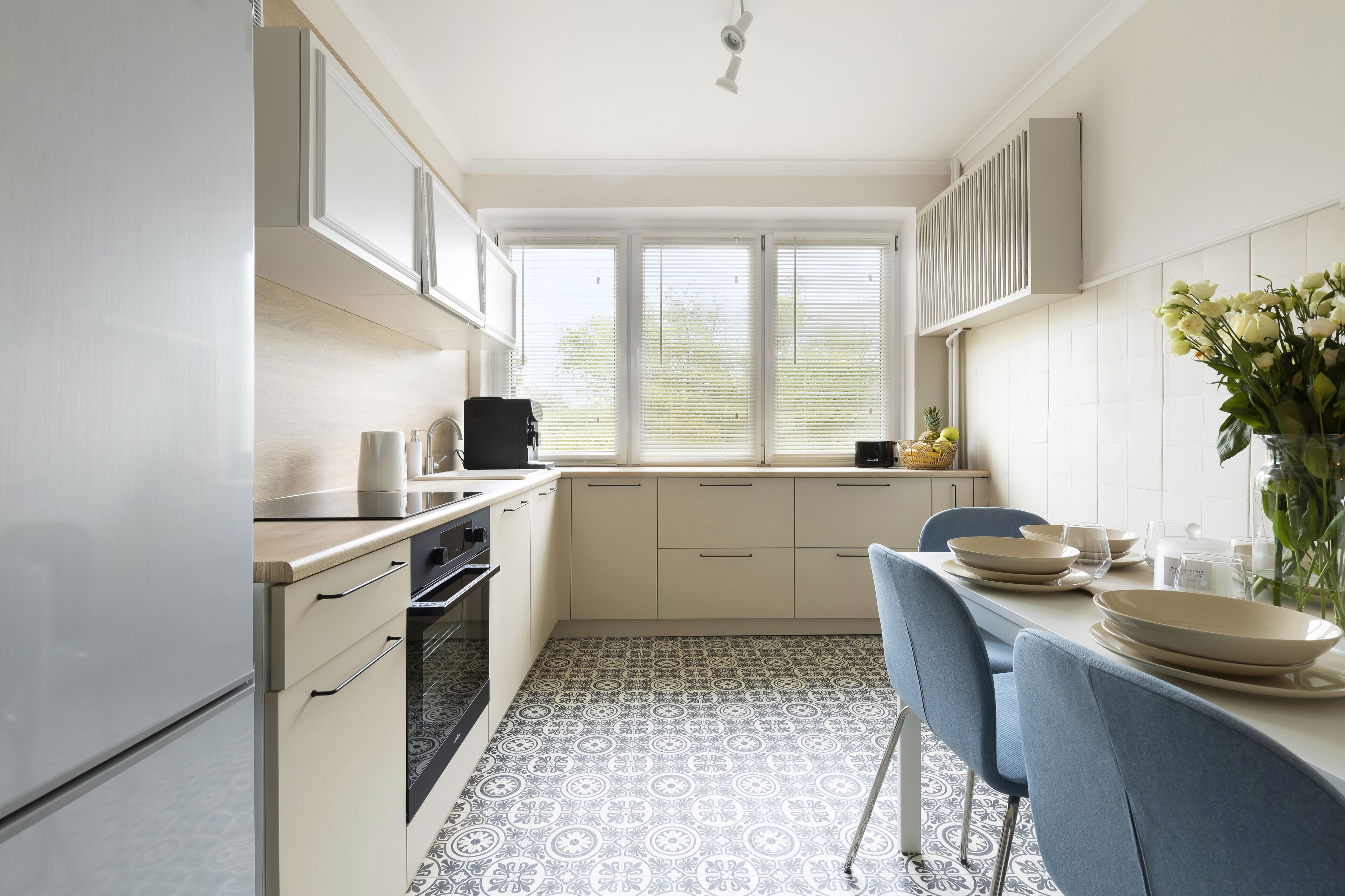 A compact kitchen with white cabinets, a built-in oven, and a dining area with blue chairs and a table set for four.