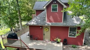 A red single-story house with a porch, a covered grill, and a small garden area.