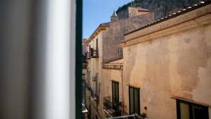 A narrow street with buildings, a visible balcony, and a mountain in the background. - KALEA Guest House (Cefalù)