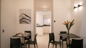 A dining area with a table and chairs, a vase with flowers, and a kitchen in the background. - KALEA Guest House (Cefalù)