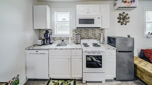 A compact kitchen with white cabinets, a microwave, a stove, a dishwasher, and a refrigerator. - Cozy Tiny Homes Green (Rhome)