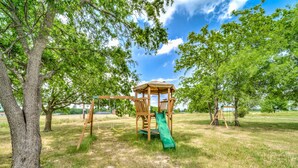A wooden play structure with a slide and swings in a grassy park area. - Cozy Tiny Homes Green (Rhome)