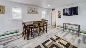 A dining area with a wooden table and chairs, a TV mounted on the wall, and a door leading to another room. - Cozy Tiny Homes Green (Rhome)