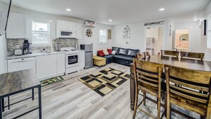 A modern kitchen with white cabinets, a dining area with wooden chairs, and a black leather sofa. - Cozy Tiny Homes Green (Rhome)