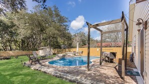 En baghave med swimmingpool, havemøbler og pergola.