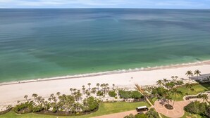 Een luchtbeeld van een strand met helder water, een zandstrand en palmbomen.