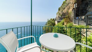 Un balcón con una mesa y silla blancos, con vistas a un acantilado y el mar.