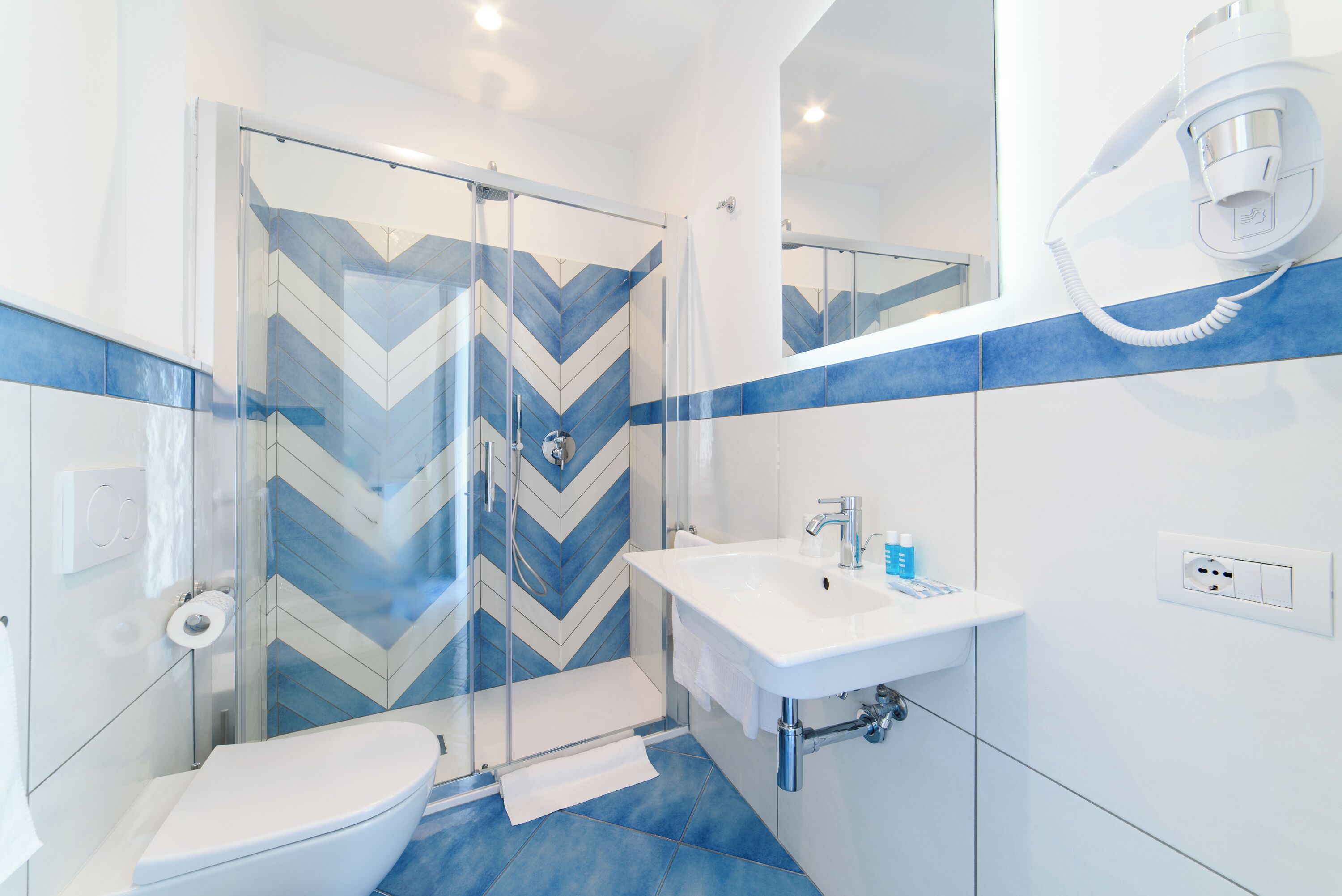 Un baño moderno con cabina de ducha de vidrio, un lavamanos blanco y un inodoro.