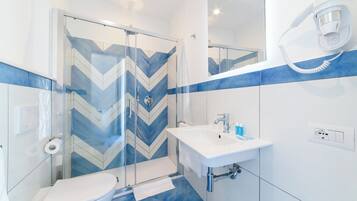 Un baño moderno con cabina de ducha de vidrio, un lavamanos blanco y un inodoro.
