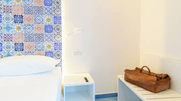 A neatly arranged hotel room with a bed, a small bedside table, a bench, and a wall with colorful tiles.