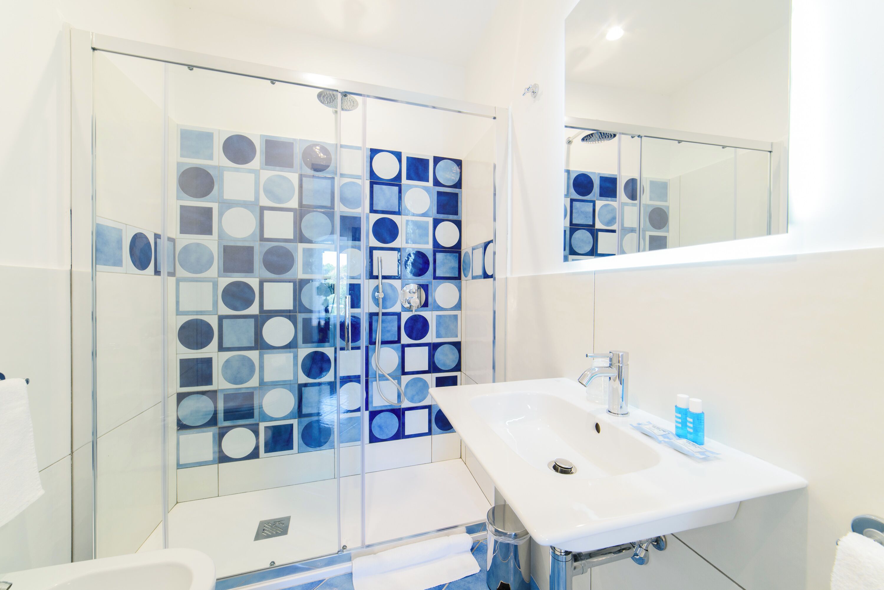A modern bathroom with a glass shower enclosure, a white sink, and a mirror.