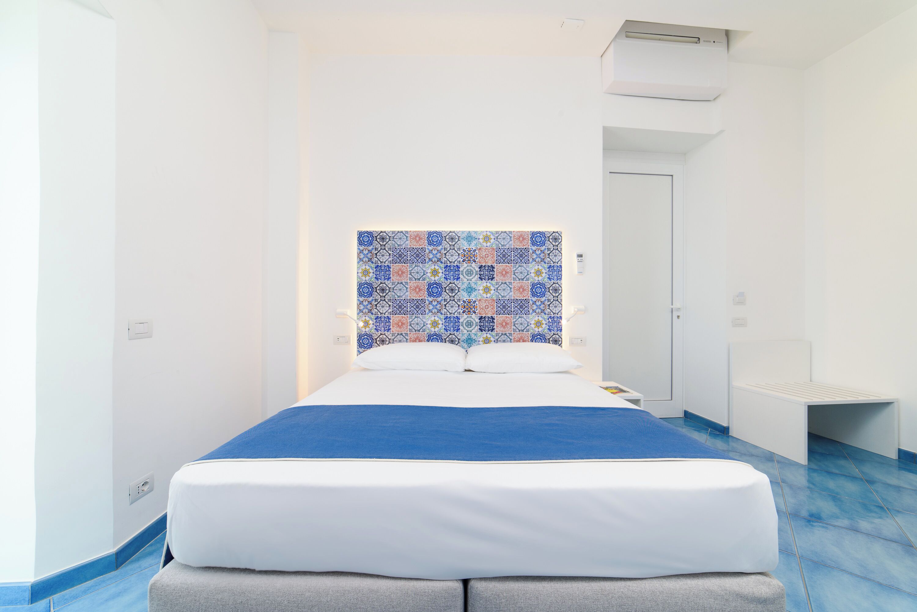 Ein modernes Hotelzimmer mit einem ordentlich bezogenen Bett, einer blauen Akzentwand und einem gemusterten Fliesen-Kopfteil.