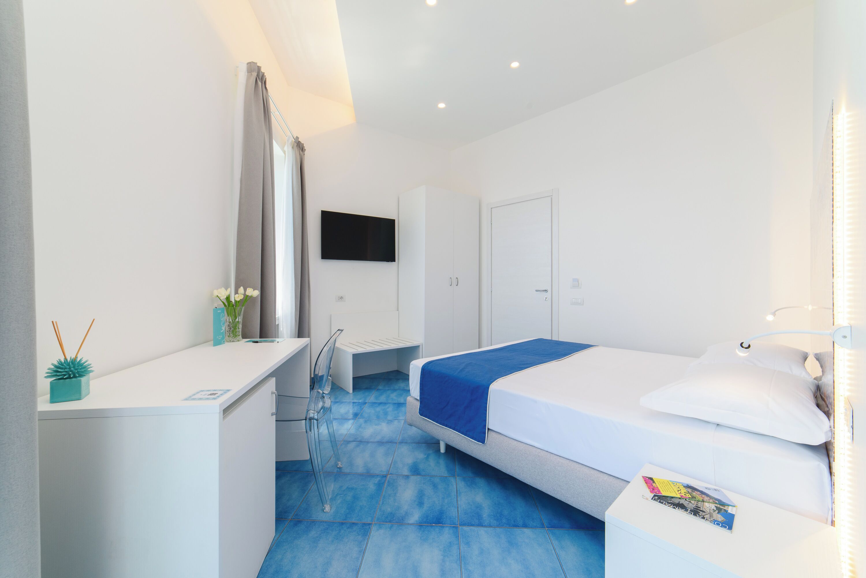A modern hotel room with a bed, a desk, a chair, a TV, and a bathroom.