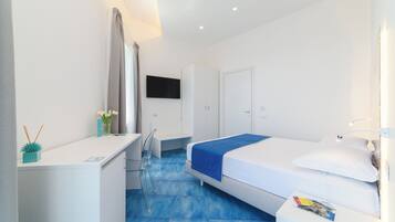 A modern hotel room with a bed, a desk, a chair, a TV, and a bathroom.