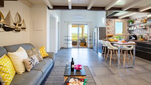 A modern living room with a sofa, coffee table, and dining area with chairs. There is a kitchen in the background with a counter and shelves. - I Mandorli - Lovely loft in Sardinia (Loceri)