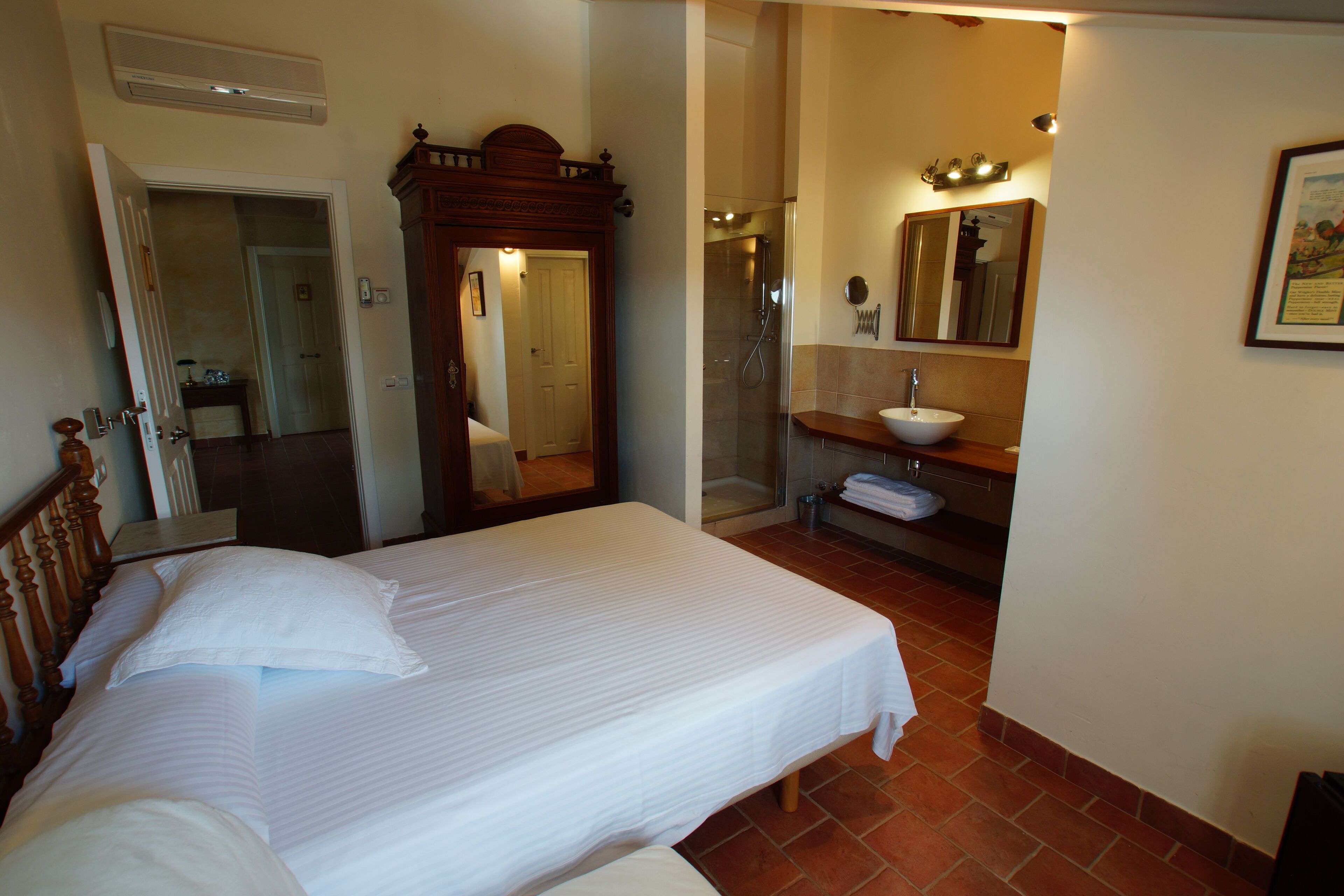A hotel room with a bed, a bathroom with a sink and mirror, and a shower.