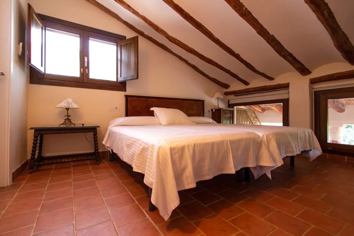 A bedroom with two beds, a nightstand, a lamp, and a window.