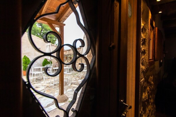A doorway with a wrought iron design, leading to an outdoor patio area with stone flooring and white metal chairs. - Torre alta de Ram (Alcaniz)