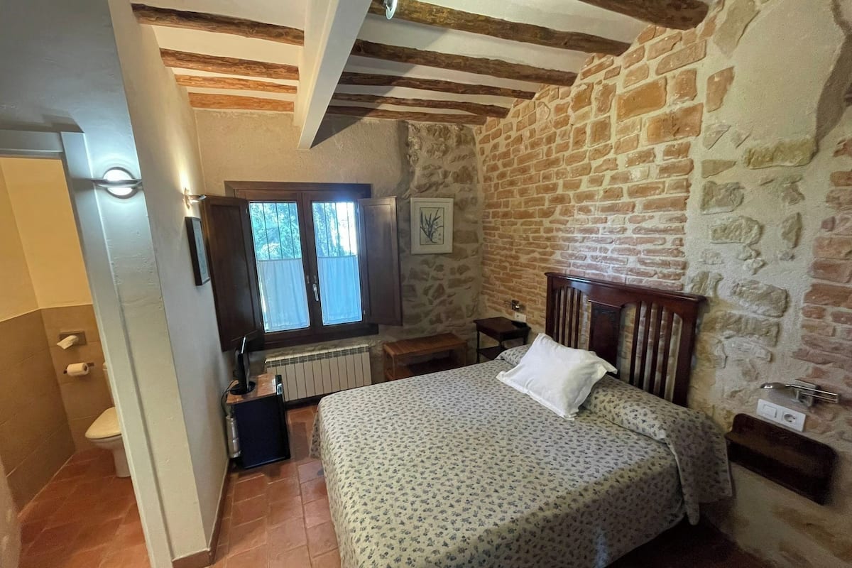 A bedroom with a bed, wooden headboard, stone wall, and a window with curtains.