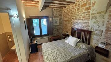 Un dormitorio con cama, cabecera de madera, pared de piedra y ventana con cortinas.