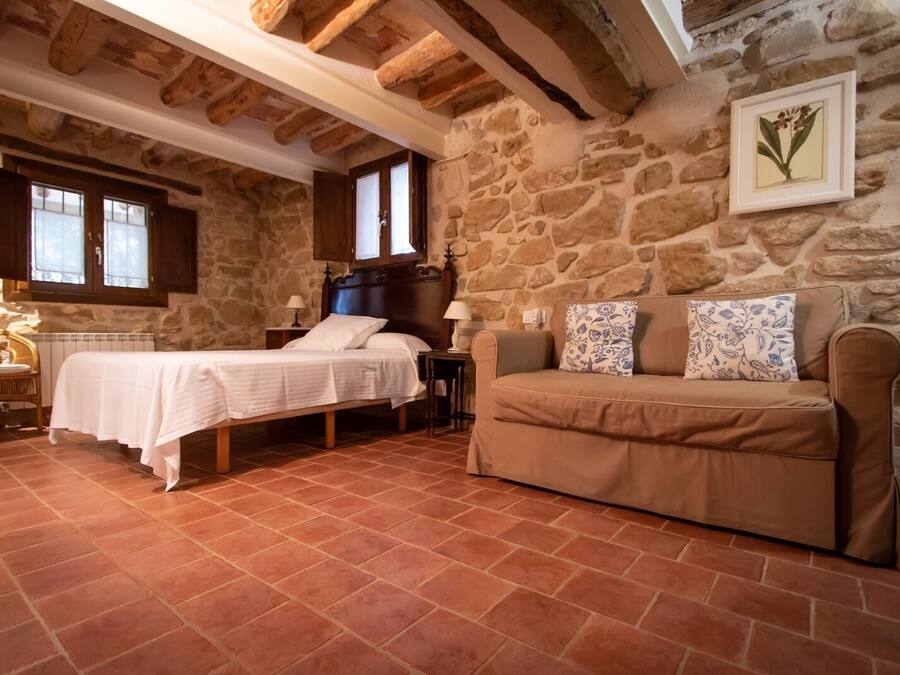 A rustic bedroom with a stone wall, a wooden bed, a brown sofa, and a small table.