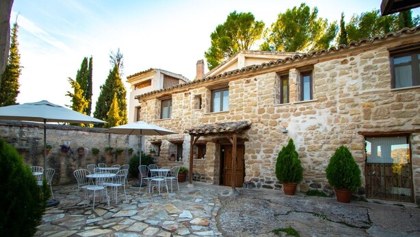 A stone building with a courtyard, outdoor seating, and potted plants. - Torre alta de Ram (Alcaniz)
