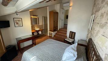 Un dormitorio con cama, cabecera de madera, mesita de noche, escritorio, silla, espejo, lavabo y ducha.