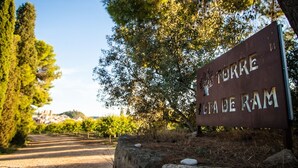 A sign with the text "TORRE ALTA DE RAM" in a natural setting with trees and a clear sky. - Torre alta de Ram (Alcaniz)