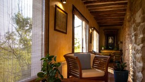A cozy indoor seating area with a wooden ceiling, stone walls, and a large window with blinds. - Torre alta de Ram (Alcaniz)