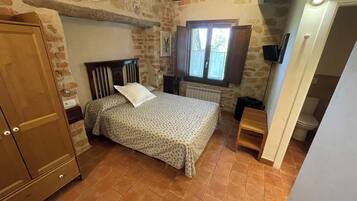 Un dormitorio con cama, armario de madera, pared de piedra, ventana y radiador.