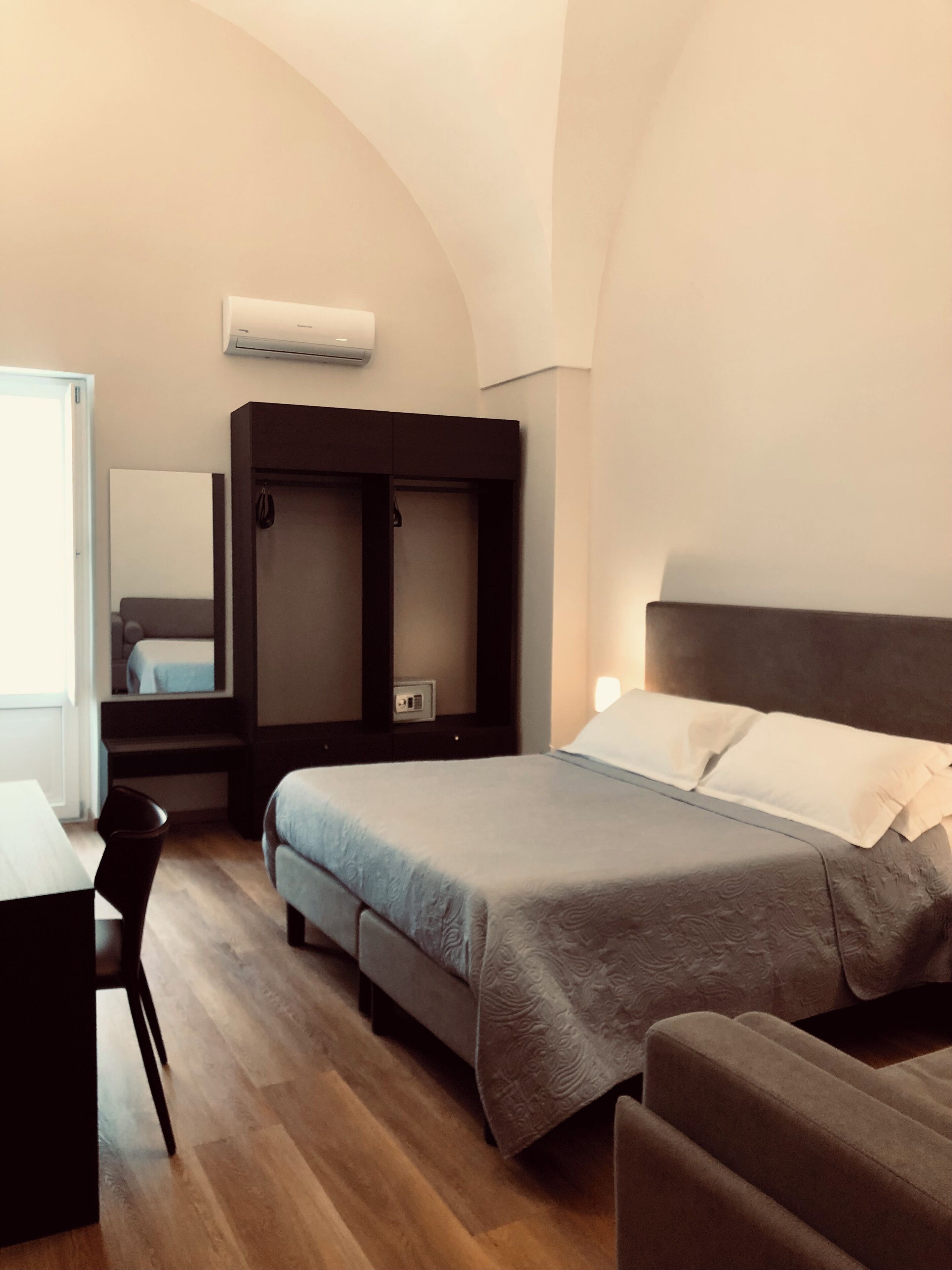 A modern hotel room with a bed, a desk, and a wardrobe.
