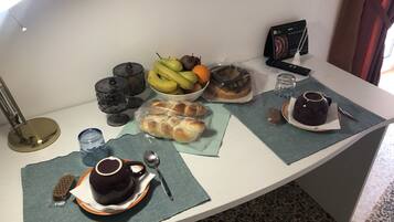 A breakfast setup with bread, fruits, a coffee pot, and a remote control on a table.