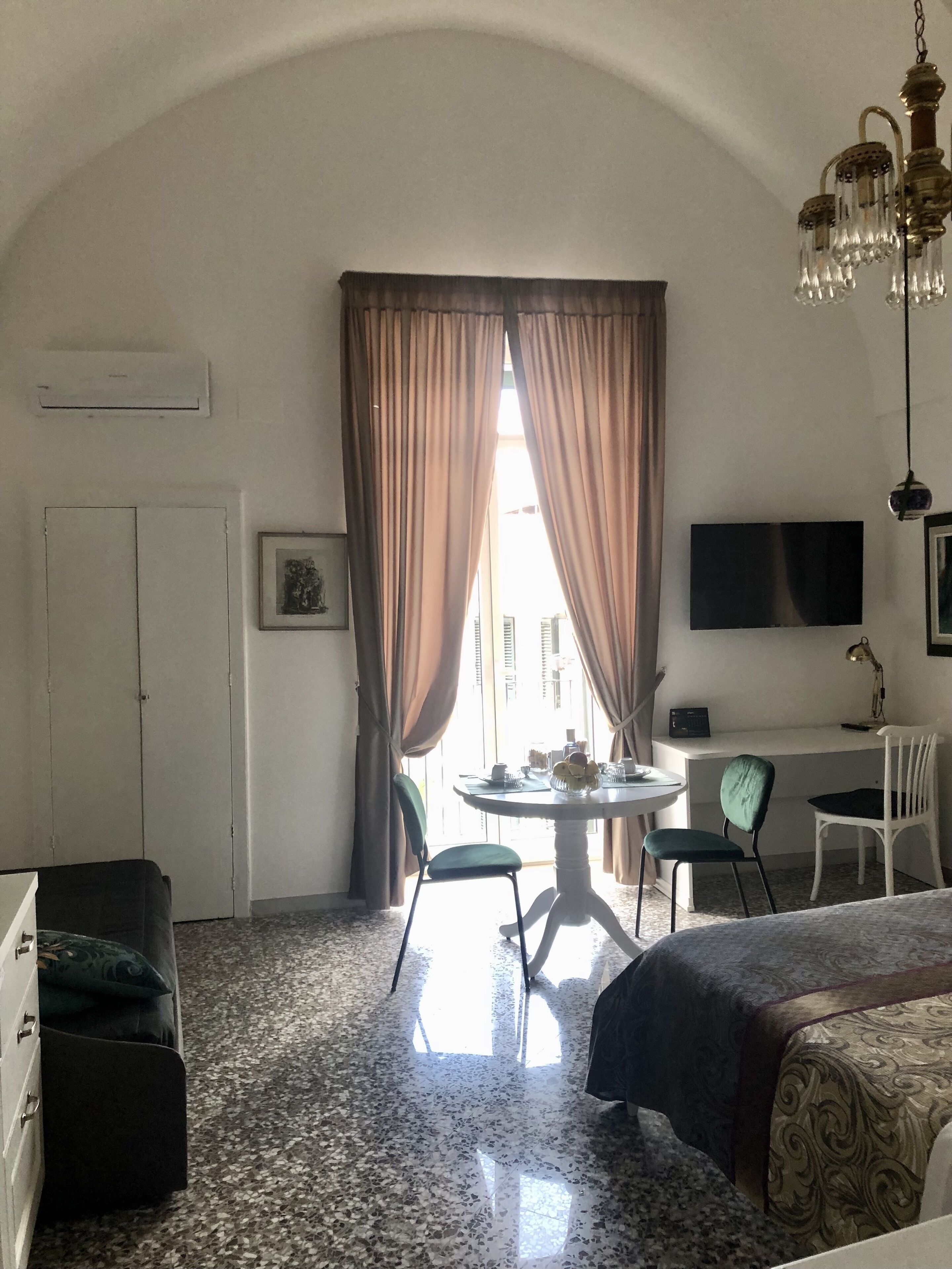A hotel room with a bed, a desk with a chair, a TV, and a dining table with chairs.