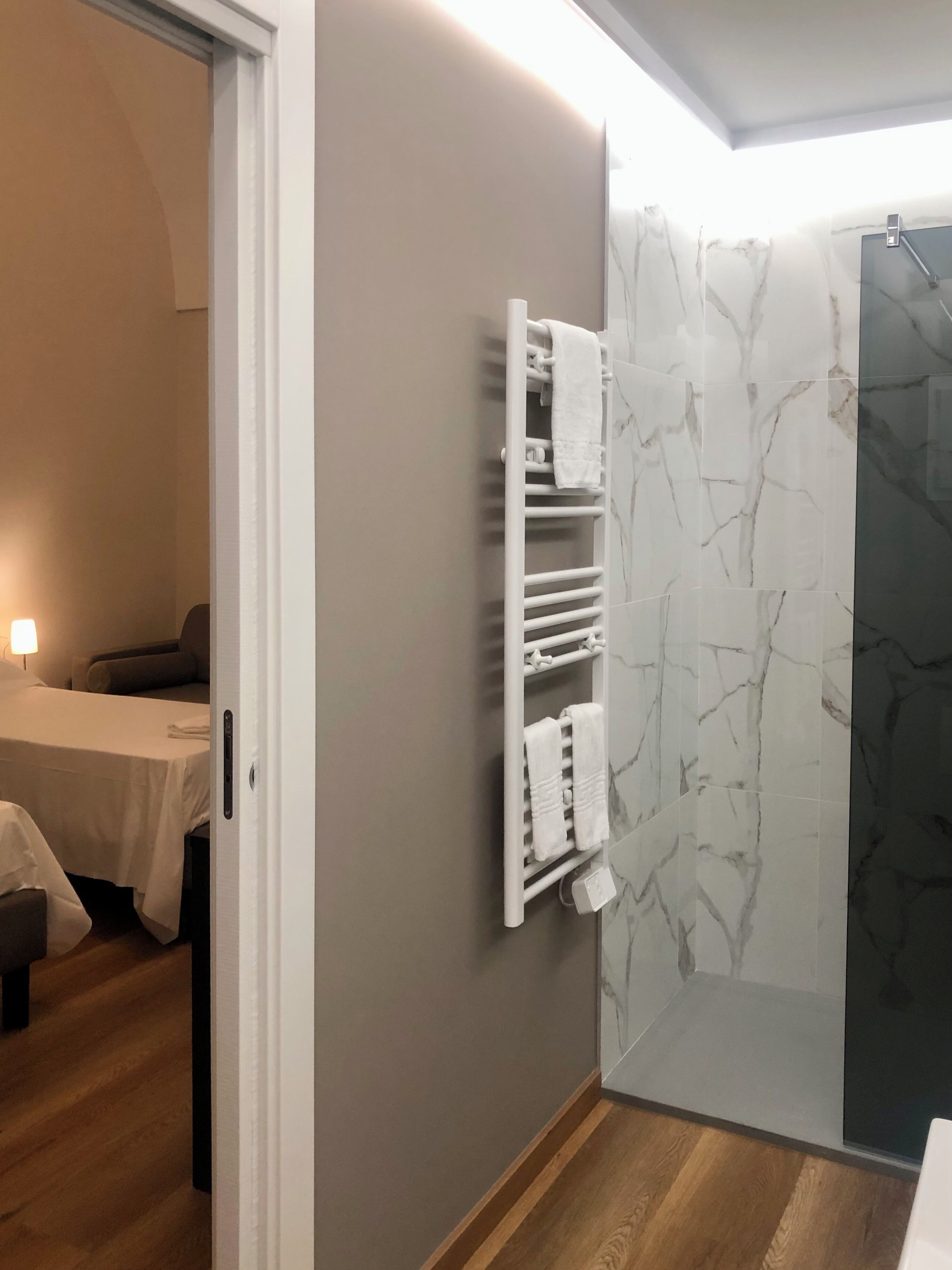 Une chambre d’hôtel comprenant un lit, une table de chevet, un porte-serviettes fixé au mur et un espace douche avec des carreaux de marbre.